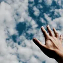 a hand reaching towards a cloudy sky