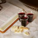 An open Bible with small cup of wine and unleavened bread.