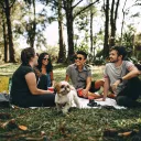 four young people and a dog outdoors on a picnic mat in a field