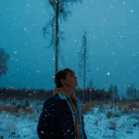 a man standing outside in the snow with snowflakes falling against a darkened sky