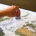 a hand reaching into a plastic container of colorful pins sitting atop a world map