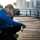 A man sitting on a dock with the water near by.