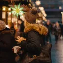 A woman standing in line surrounded by people and Christmas lights.