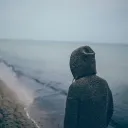 A person wearing a hoodie looking at the waves of the ocean.