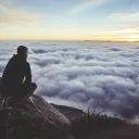 A man sitting on a rock looking out over the clouds covering a valley.