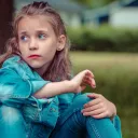 A little girl sitting on the grass looking sad.