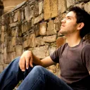 A young man sitting against a rock wall.