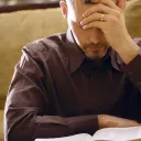 A man with his hand holding his head while looking down at a Bible.