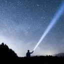 A person shining a flashlight up into the night sky.
