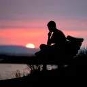 Uma pessoa sentada em um banco vendo o pôr do sol.