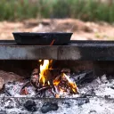 A cast iron skillet on a fire grate with hot flames underneath.