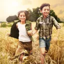 Two kids running through a tall grass field.