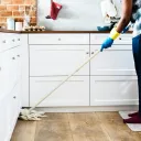 A person cleaning a kitchen floor with a mop.