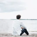 A young man sitting on the shore a lake - looking at the water.
