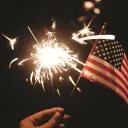A person holding a sparkler and a small American flag.