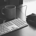 A coffee cup, keyboard and a mouse on a table.