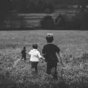 Three young boys running through a field of tall grass.