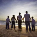 A family holding hands looking at the ocean waves and the sun setting.