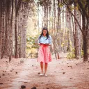 A young woman reading a book while walking on path lined by trees.