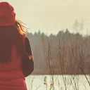 A woman wearing a jacket sitting outside looking at a lake.