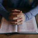 A woman praying with her hands on a Bible.