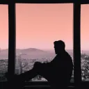 A man sitting in a window sill looking out over a city skape.