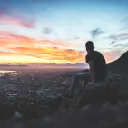 A young man sitting on a rock looking at the cityscape below.
