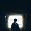 A man walking in a dark tunnel with light at the very end.