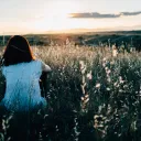 A young woman sitting in a field of grass and flowers watching the sunset.