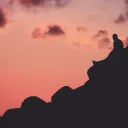 A person sitting a hill with a red sky.