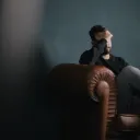 A man sitting on a chair holding his head with his hand.