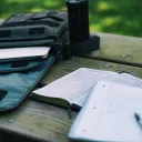 A Bible and notebook laying on a table. A laptop is in backpack.