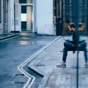 A man sitting by a building looking at his phone.