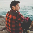A young man sitting on a rock looking out over the water.