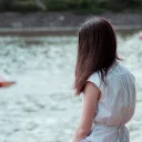A teen girl sitting by a small pond looking out over the water.