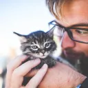 A man wearing glasses holding a kitten close to his face.