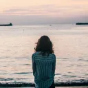 A woman sitting by a large body of water.