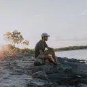 A man sitting on a log by a lake.