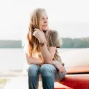 A young woman sitting on the edge of kayak that is on the shore.