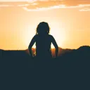 A silhouette of young woman with small mountains and a setting sun in background.