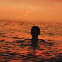 A person floating in the water with the sun setting.