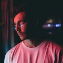 A young man staring at neon sign on a window.
