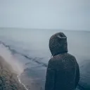 A person walking on a beach wearing a hoodie.