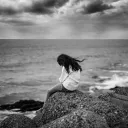 A woman sitting on a rock next to large body of water.