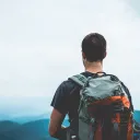 A guy wearing a backpack at the top of a hill.