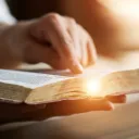 An open Bible with someone's hand pointing to a scripture.