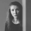 A young woman looking from behind an edge of a wall.