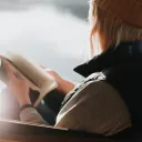 A woman sitting by a lake paging through a Bible.