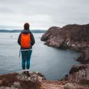 A woman hiking and standing on a cliff over looking a lake.