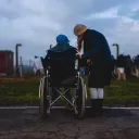 A woman helping an elderly person in a wheelchair.